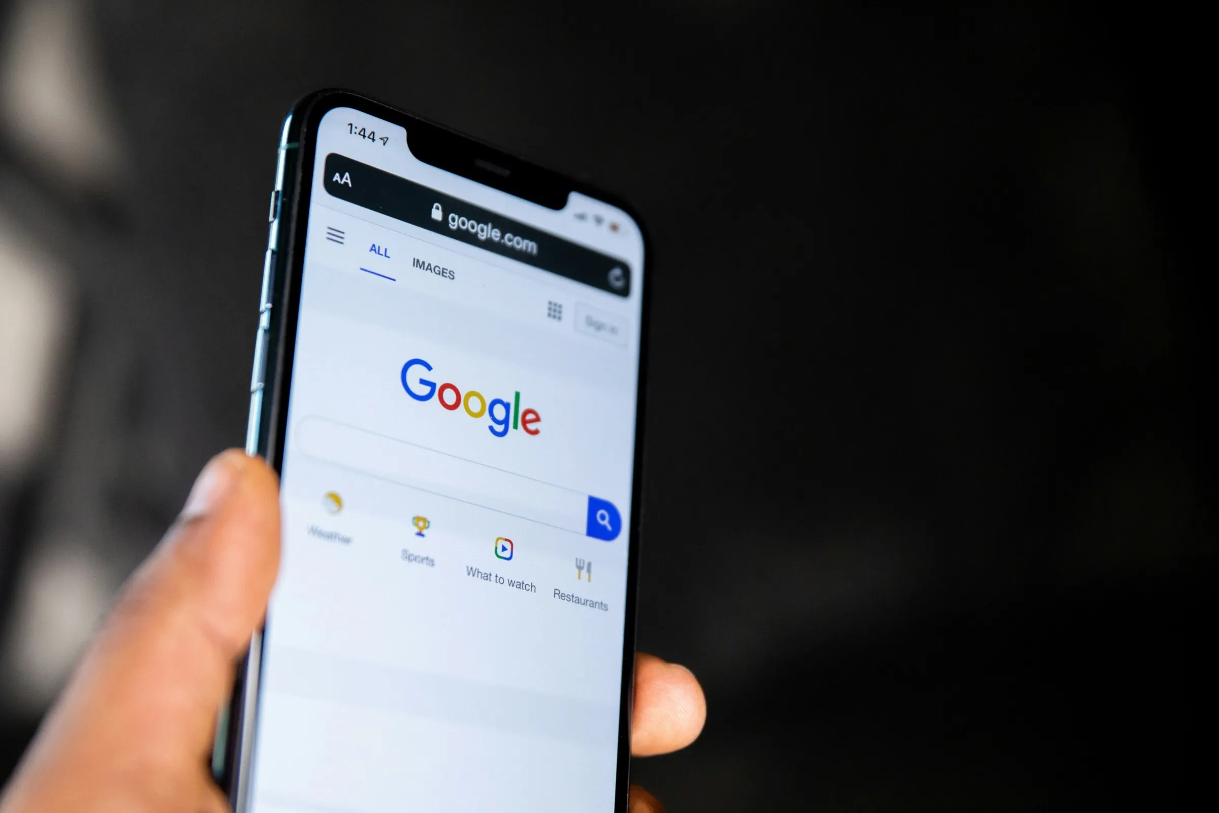 Ruka drží telefon s otevřeným vyhledávačem Google