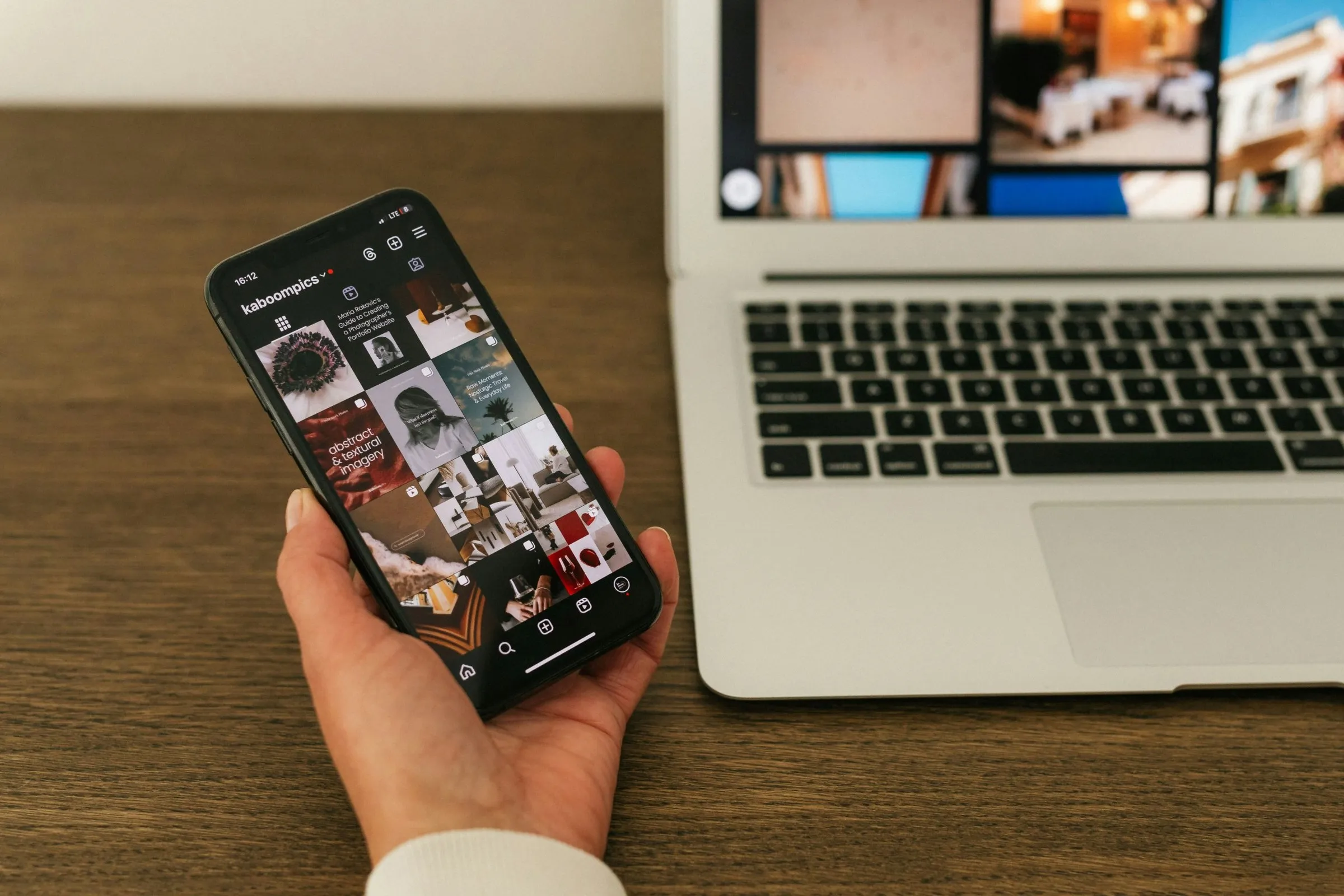 Ruka drží telefon s profilem na Instagramu vedle otevřeného notebooku